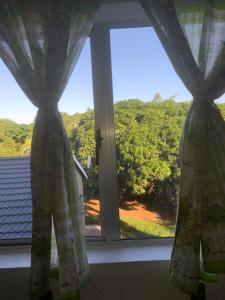 een raam met gordijnen en uitzicht op een tuin bij Modern Rustic Durban Apartment in Durban