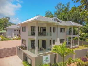 a large white building with trees in the background at Palm Holiday Apartments in Grand'Anse Praslin