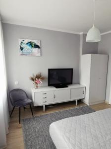 a white bedroom with a tv and a chair at Apartament z widokiem na jezioro Ukiel in Olsztyn