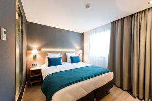 a hotel room with a large bed with blue pillows at Golden Tulip Sophia Antipolis - Hotel & Spa in Valbonne