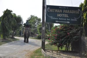 an elephant walking down a road with a sign at Chitwan Paradise Hotel in Sauraha