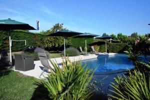 uma piscina com duas cadeiras e guarda-sóis num quintal em The Originals City, Hôtel du Phare, Bordeaux Mérignac (Inter-Hotel) em Mérignac