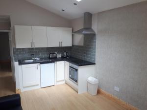 a kitchen with white cabinets and a black tile wall at One double bedroom flat in Dublin