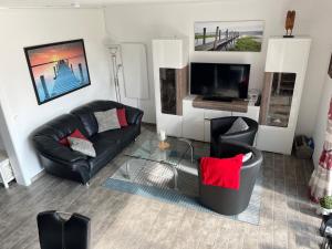 a living room with black leather furniture and a flat screen tv at Gleich hinterm Deich 4 in Friedrichskoog