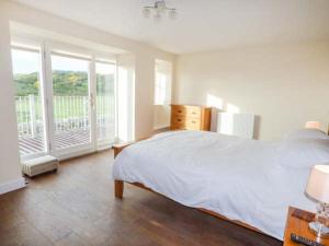 a white bedroom with a bed and a balcony at Ysgubor Newydd in Cemaes Bay