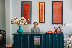 une femme debout derrière une table avec un vase de fleurs dans l'établissement Heritage Boutique Sierra Legend, à Nha Trang