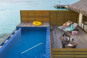 a woman sitting on a deck next to a swimming pool at Cocoon Maldives - All Inclusive in Lhaviyani Atoll