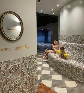 two children sitting on a couch in a lobby with a mirror at Citrus SPA Hotel in Jēkabpils