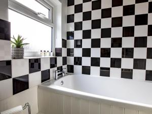 een badkamer met een bad en een zwart-witte geruite muur bij Pass the Keys Central cosy home 5 minutes walk from Shrewsbury in Shrewsbury +14 foto's