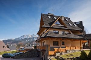 a house with a black roof with mountains in the background at Apartament Sywarne Deluxe in Kościelisko