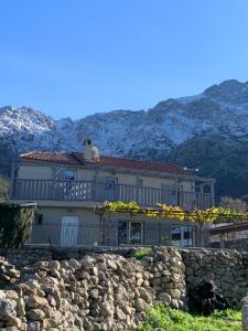 une maison derrière un mur en pierre avec des montagnes en arrière-plan dans l'établissement Casa Basgiu, chambres avec balcon, à Zilia