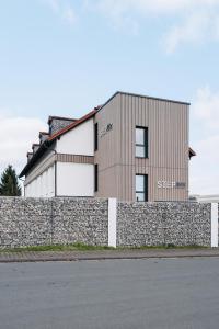 a building behind a stone retaining wall with a fence at STEP INN The Fair Hotel in Rosbach vor der Höhe