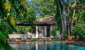 a pool with chairs and an umbrella next to a house at Haritha Villas & Spa in Hikkaduwa +29 photos