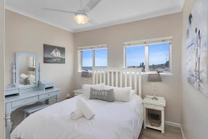 a bedroom with a white bed with a desk and windows at Driftwood 15 in Ballito