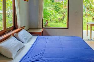 a blue bed in a bedroom with two windows at Dina Home Stay at Desa Wisata Wongayagede in Jatiluwih