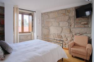 1 dormitorio con pared de piedra, 1 cama y 1 silla en Casa De Igarei, en Igarei