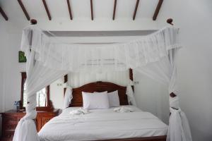 a white canopy bed with white sheets and pillows at JungleRiverHouse in Bukit Lawang