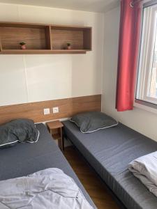 a bedroom with two beds and a window with red curtains at Mobilhome Sables du midi in Valras-Plage +25 photos