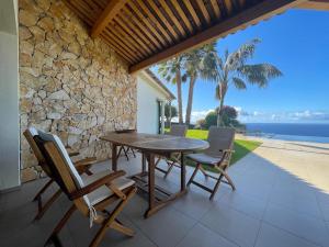 a wooden table and chairs on a patio with a stone wall at Morning Star Villa in Arco da Calheta