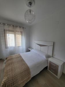 een witte slaapkamer met een bed en een kroonluchter bij Piso termal III in Ourense