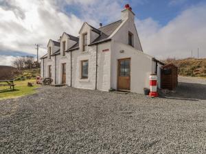 una pequeña casa blanca con entrada de grava en Red Chimneys Cottage en Husabost