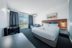 um quarto de hotel com uma grande cama branca e uma secretária em The Select Inn Ryde em Sydney