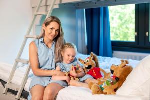 a woman sitting on a bed with a baby and stuffed animals at Original Sokos Hotel Seurahuone Kotka in Kotka