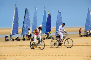 dwie osoby jeżdżące rowerami na plaży z żaglówkami w obiekcie Belambra Clubs Colleville-sur-Mer - Omaha Beach w mieście Colleville-sur-Mer