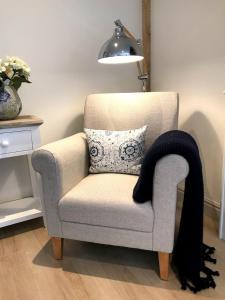a gray chair with a pillow and a lamp at STABLES Stylish comfortable peaceful cottage with parking and outdoor space in Holt