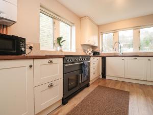 una cocina con armarios blancos y horno negro en Bronte View Cottage, en Keighley