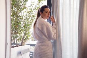 Una mujer con un vestido blanco mirando por la ventana en Cityzoe Athens Suites, en Atenas