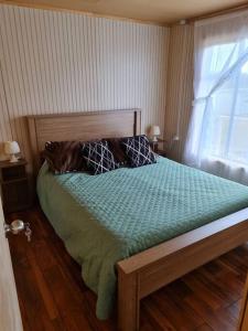 ein Schlafzimmer mit einem Bett mit einer grünen Bettdecke und einem Fenster in der Unterkunft Cabaña Nothofagus PUQ in Punta Arenas