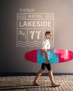 Ein Mann läuft die Straße entlang und hält ein Surfbrett. in der Unterkunft Lakeside77 in Podersdorf am See