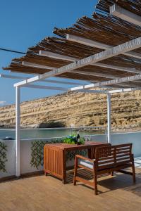 een houten tafel en een bank onder een pergola bij Flores Playa in Matala