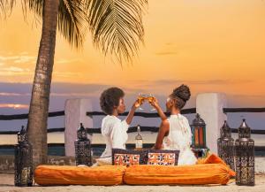 dos personas sentadas en un barco en la playa bebiendo cerveza en Zanzibar Beach Resort en Zanzíbar
