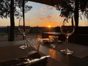 two wine glasses sitting on a table with the sunset at Agriturismo con cucina Il Favaio in Paciano