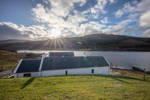 a house on the shore of a lake with the sun shining at Shore Cottage Isle of Skye in Portree