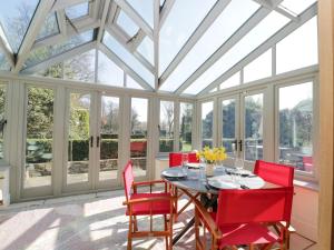 a conservatory dining room with a table and red chairs at Rose Cottage in Corsham