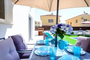 a table with blue glasses and a vase with purple flowers at Voroklini Villa with Pool in Larnaka