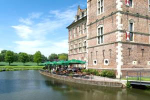 a building with tables and green umbrellas next to a river at Schloss Raesfeld in Raesfeld