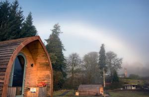 een houten schuur met een deur in een veld bij Luxury Rural Ayrshire Glamping Pod in Dalmellington