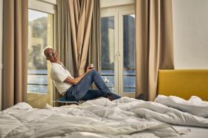 un homme assis dans une chaise à côté d'un lit dans l'établissement Hotel Paradiso Conca d'Oro, à Nago-Torbole