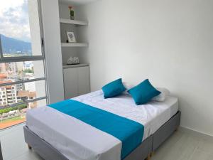 a bed with blue pillows in a room with a window at Apartamento Nuevo Hermosa Vista in Ibagué