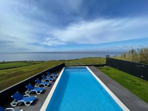 a swimming pool with chairs and the ocean in the background at Vivenda Luxuosa in Feteiras