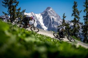 two people riding bikes down a hill with a mountain in the background at ALM SEASONS Premium Chalet & Studios in Saalbach-Hinterglemm