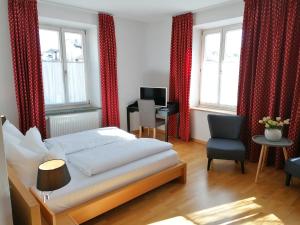 a bedroom with a bed and a chair and windows at Hotel Wendelstein in Rosenheim