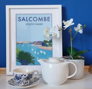 a table with two cups and a vase and a picture at Merrifield House Devon in Kingsbridge