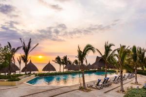 a resort pool with chairs and palm trees and the ocean at Dreams Karibana Cartagena Golf & Spa Resort in Cartagena de Indias