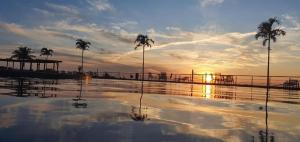 uma piscina de água com palmeiras e o pôr do sol em Apart-Hotel Golden Lake 2 em Arraial do Cabo