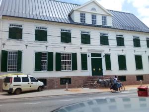 a white building with green shutters and a person on a bike at 3 Bed House - Sleeps 4 - Parking - Enclosed Garden in Paramaribo